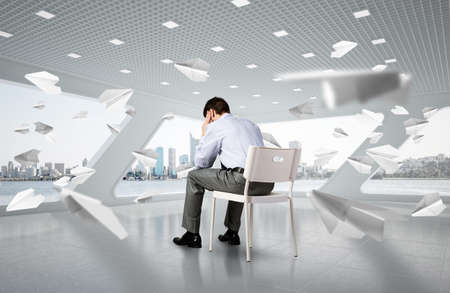 young businessman sitting on a chair with his head in his handsの写真素材