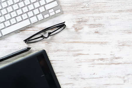 Top view office workspace composition. Flat lay wooden desk with pc keyboard, glasses and graphic tablet. Design and creativity. Time management and planning. Designer workplace organization.の写真素材