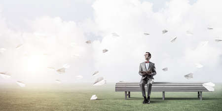 Funny man in red glasses and suit sitting on bench and reading bookの写真素材