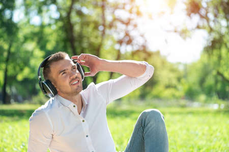 Young man in the park listens to music. He sits on the grass and enjoys music.の写真素材