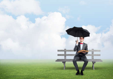 A young student holds a book and an umbrella. sits on a wooden benchの写真素材