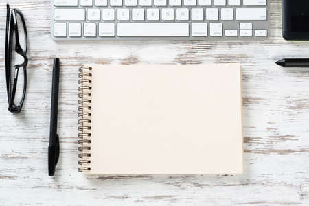 Still life of office workspace with supplies. Flat lay wooden desk with white computer keyboard,...