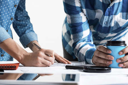Woman writing with pen on technical drawing. Creative team of designers together working with...