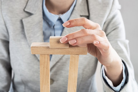 Business woman building tower on table from wooden blocks. Business development and assistance concept. Young woman wearing formal wear sitting in office interior. New challenge and leadershipの写真素材