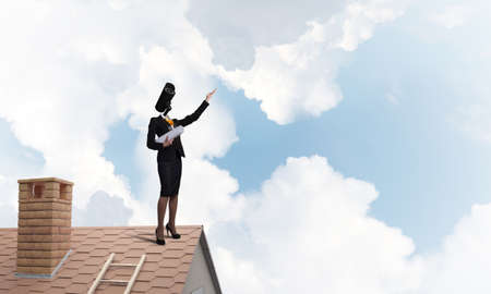 Faceless businesswoman with camera zoom instead of head standing on house roofの写真素材