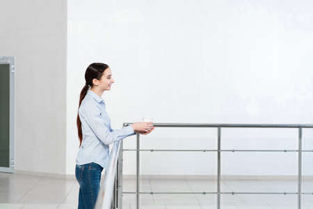 young attractive woman with a paper cup of coffee, rests on railingの写真素材