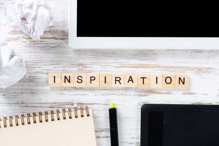 Inspiration and motivation concept with letters on cubes. Still life of workspace with supplies. Flat lay wooden desk with tablet computer and spiral notebook. Brainstorming and ideas generationの写真素材