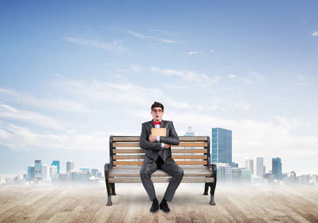 Student sits on a bench, holding a book. Traditional education conceptの写真素材