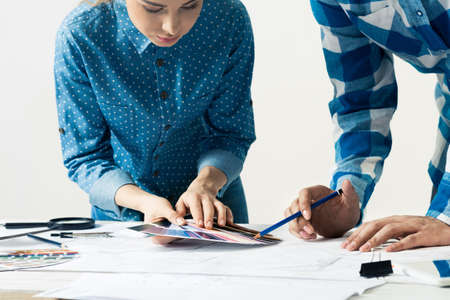 Interior designers discussing color samples for design project. Close up man hand with pencil pointing on color palette. Professional building, decoration and renovation. Teamwork and creativityの写真素材