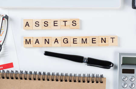 Asset management concept with letters on cubes. Still life of office workplace with supplies. Flat lay white surface with tablet computer, calculator and notepad. Investment strategy and planning.の写真素材