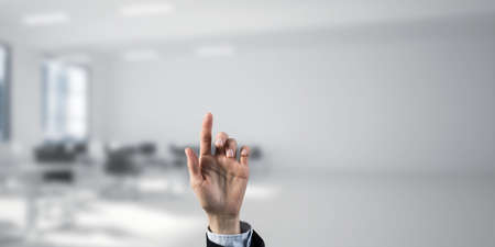Close of businesswoman hand touching screen with finger and office at backgroundの写真素材