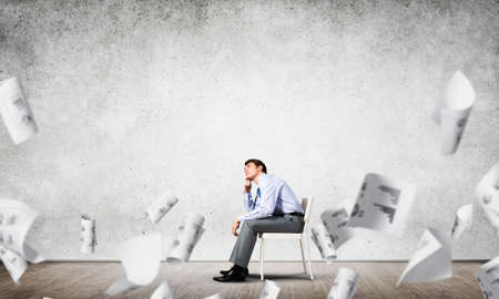 young businessman sits on an office chair, thoughtful and looking upの写真素材