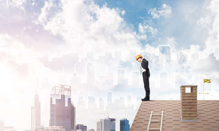 Young businessman in suit and helmet on roof edge. Mixed mediaの写真素材