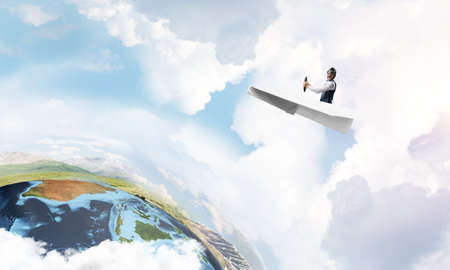Aviator having fun in aircraft. Pilot in leather helmet and goggles driving paper plane in cloudy...