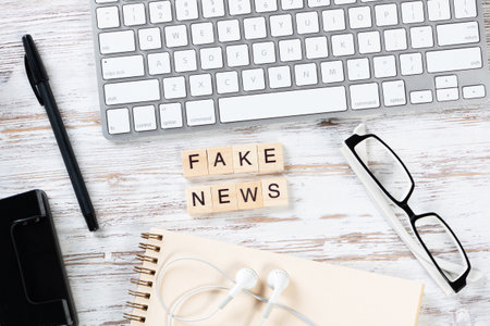 Fake news concept with letters on cubes. Flat lay vintage wooden desk with computer keyboard, headphones, and notebook. Disinformation media technology. Still life of journalist workplace.の写真素材