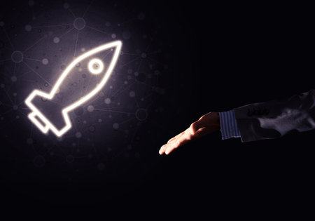 Rocket glowing icon and businessman hand on dark background