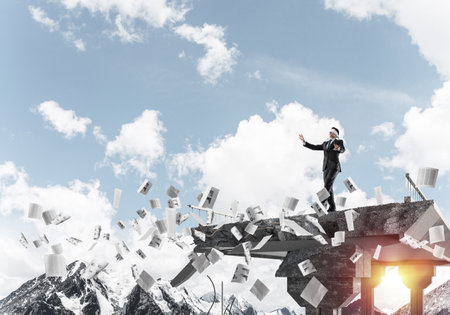 Businessman walking blindfolded among flying documents on concrete bridge with huge gap as symbol of hidden threats and risks. Skyscape and nature view on background. 3D rendering.の写真素材