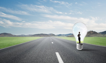Young businesswoman trapped inside of light bulb on asphalt roadの写真素材