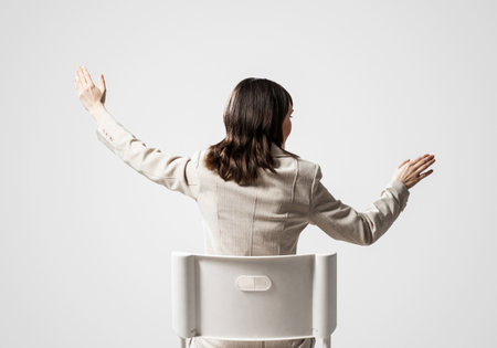 Woman gesturing or something showing in air. Back view long haired woman in white suit sitting on white chair. Business concept with copy space. Template for advertising and promotion campaignの写真素材