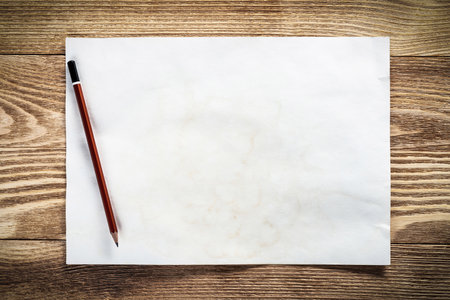 Artist workplace with sheet of paper and pencil lying on wooden desk. Rectangular white paper with blank copy space. Textured natural wooden background. Art school template for advertising.の写真素材