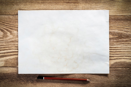 Sheet of paper lying on wooden table. Blank white a4 format paper with pencil. Space for writing and notification. Textured natural wooden background. Vintage copy space for creative design.の写真素材