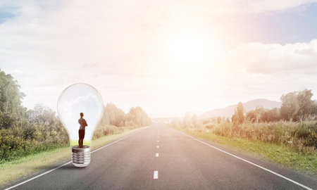 Young businesswoman trapped inside of light bulb on asphalt roadの写真素材