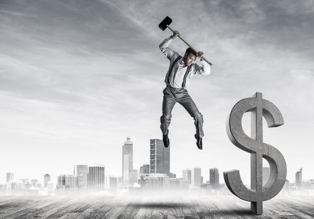 Young furious businessman going to crash with hammer stone dollar symbolの写真素材