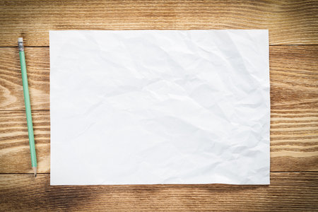 Sheet of paper lying on wooden table. Blank white a4 format paper with pencil. Textured natural wooden background. Vintage copy space for design. Business planning and idea generation.の写真素材