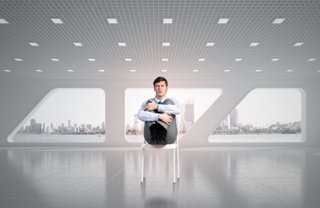 scared businessman sitting on a chair with his hands clasped his kneesの写真素材