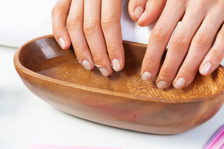 Woman hands in wooden bowl with water. Spa procedure and relaxation. Female hands preparing for manicure. Professional nail care and beautician service. Beauty and healthy lifestyle.の写真素材
