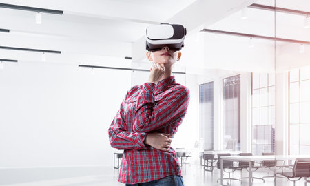 Young caucasian woman in modern office interior trying virtual reality helmet. Mixed mediaの写真素材