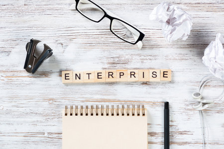 Enterprise concept with letters on cubes. Still life of businessman workspace. Flat lay vintage wooden desk with pen, glasses and spiral notepad. Business consultation and entrepreneurship.の写真素材