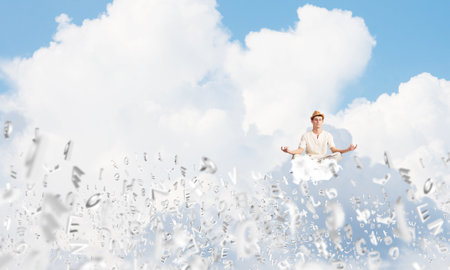 Man in white clothing keeping eyes closed and looking concentrated while meditating among flying letters in the air with cloudy skyscape on background.の写真素材