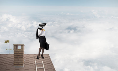 Faceless businesswoman with camera zoom instead of head standing on house roofの写真素材