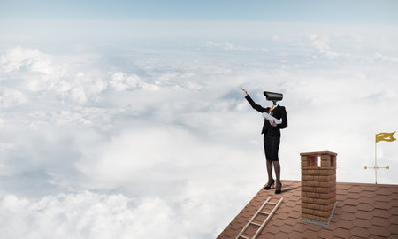 Faceless businesswoman with camera zoom instead of head standing on house roofの写真素材