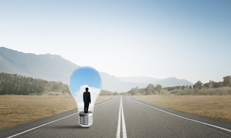 Young businessman trapped inside of light bulb on asphalt roadの写真素材