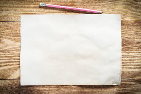 Sheet of paper lying on wooden table. Blank white a4 format paper with pencil. Textured natural wooden background. Vintage copy space for design. Business planning and idea generation.の写真素材