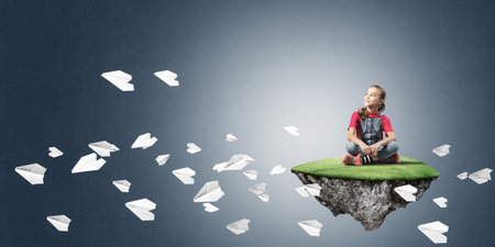 Cute smiling girl sitting on floating island and looking to the futureの写真素材