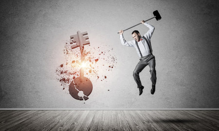 Determined businessman in empty interior breaking with hammer stone key figureの写真素材