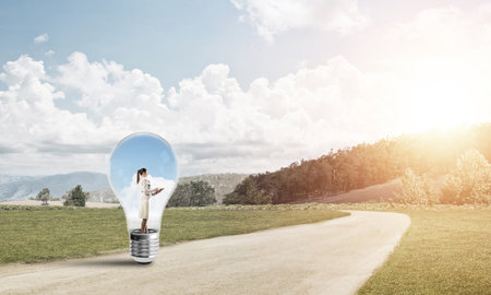 Young businesswoman trapped inside of light bulb on roadの写真素材