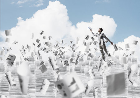 Man in casual wear keeping hand with book up while standing among flying paper documents with cloudly skyscape on background. Mixed media.の写真素材