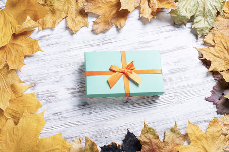Bright autumn composition with gift box and yellow maple leaves. Holiday present decorated orange ribbon bow lies on vintage wooden desk. Happy thanksgiving congratulation. Autumn sale advertising.の写真素材