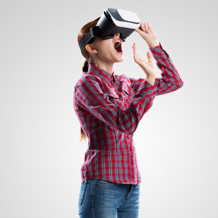 Young woman in checked shirt wearing virtual helmet against gray backgroundの写真素材