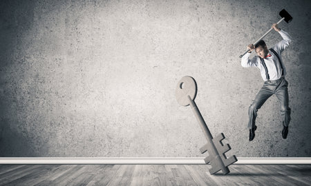 Determined businessman in empty interior breaking with hammer stone key figureの写真素材