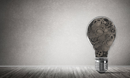 Glass lightbulb with multiple gears inside placed in empty room with grey wall on background. 3D rendering.の写真素材