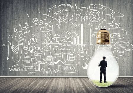 Businessman inside of light bulb in empty concrete room and sketches on wallの写真素材