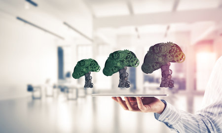 Close of businessman holding tablet pc with green tree made of gears and cogwheels. Mixed mediaの写真素材