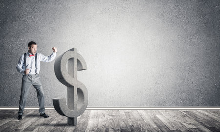 Young furious businessman going to crash with fist stone dollar symbolの写真素材