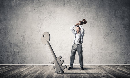 Determined businessman in concrete interior breaking with violin stone key figureの写真素材