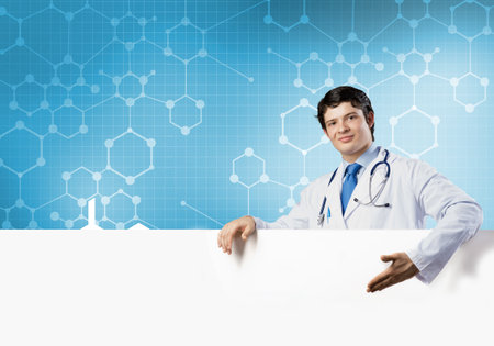 Young handsome doctor holding white blank banner. Place your textの写真素材